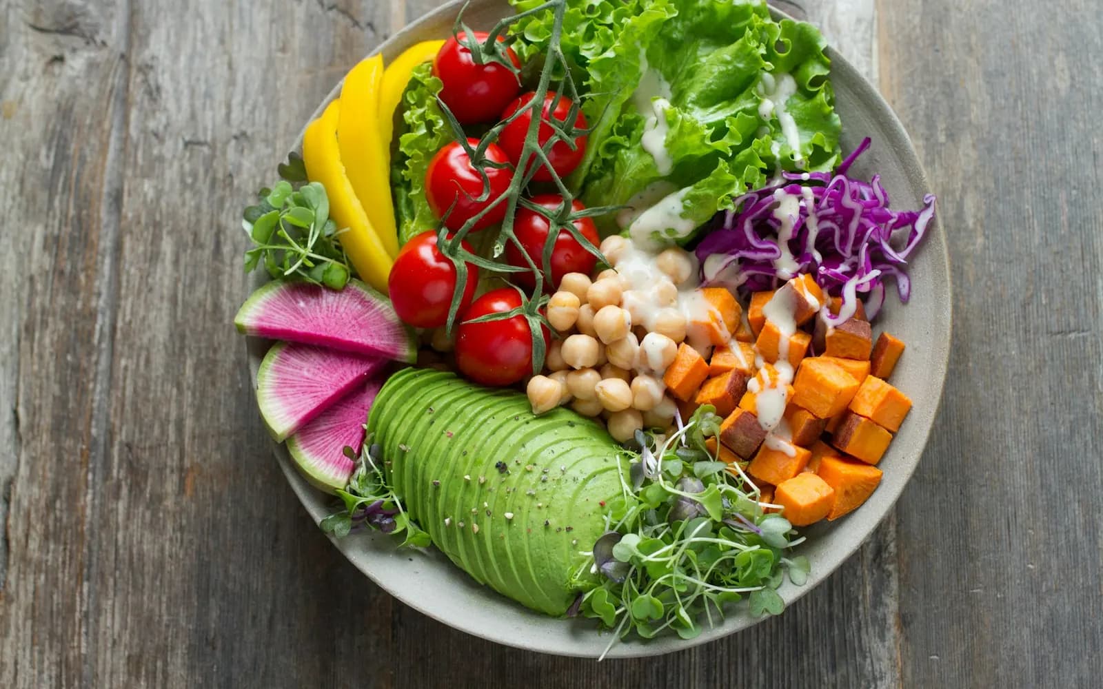 A bowl of chickpeas, avocado, sweet potato, tomatoes and greens